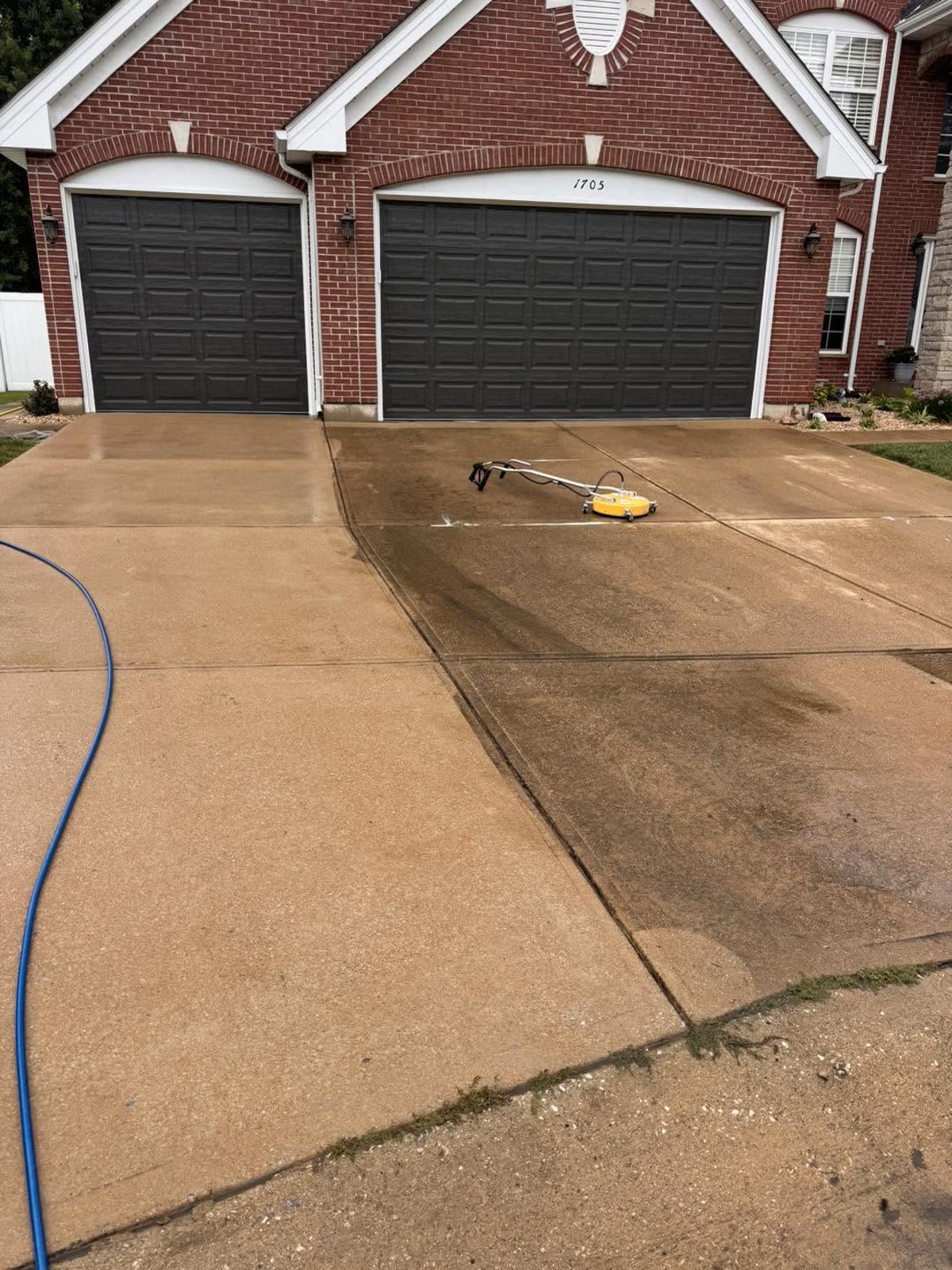 A brick home's double driveway mid-clean, a bright cleaned strip beside the dirty concrete